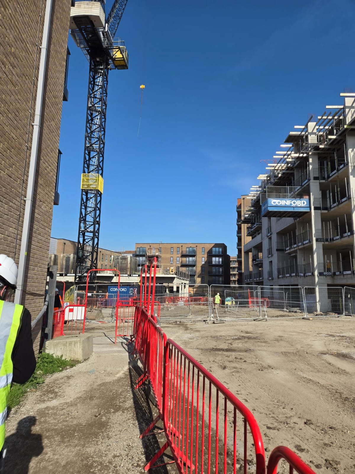 Active residential construction site with tower crane, scaffolded apartment block, and groundworks underway ahead of large-scale furniture installation.