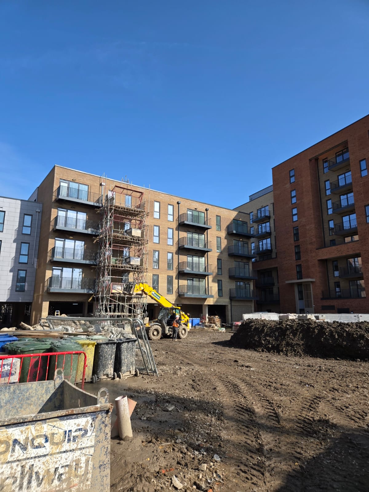 Apartment blocks on a major new-build scheme showing finished facades and live site activity around handover zones.