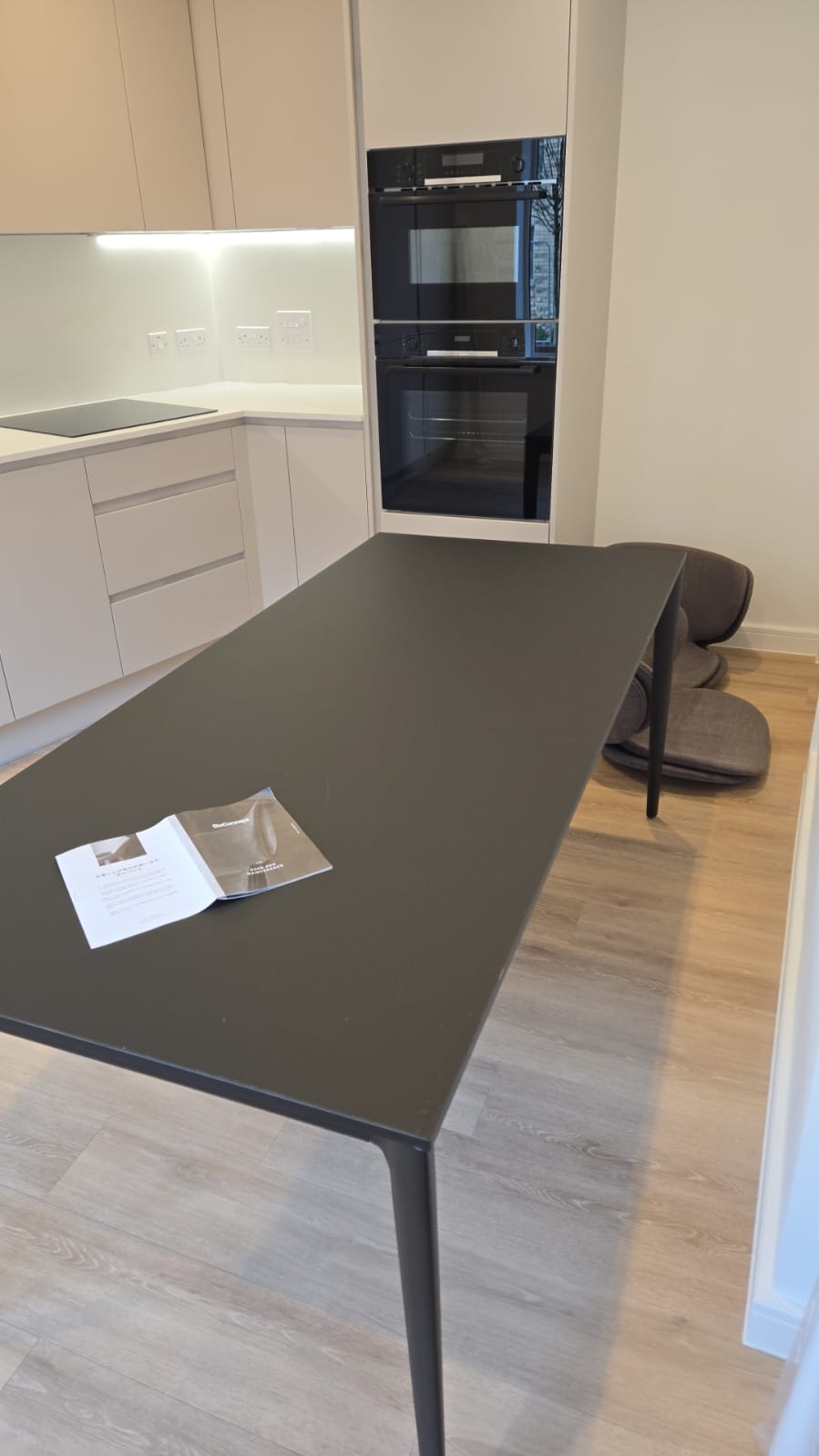 Finished kitchen and dining area with integrated appliances and furniture installed in a new apartment.