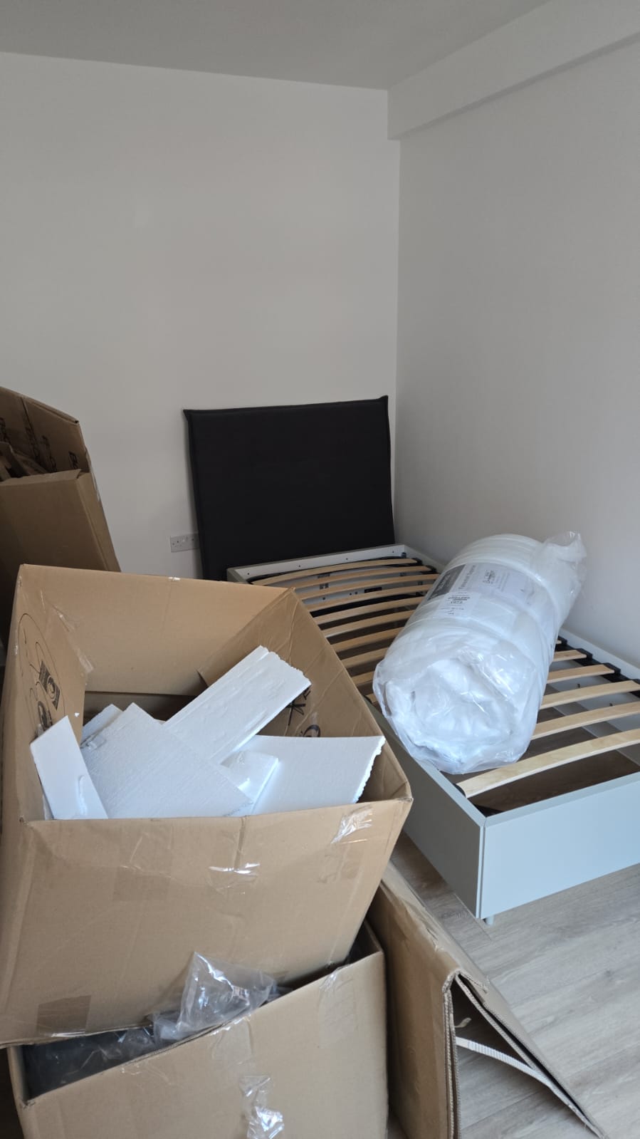 Boxed bed components and packaging inside a bedroom awaiting assembly as part of a multi-unit installation programme.